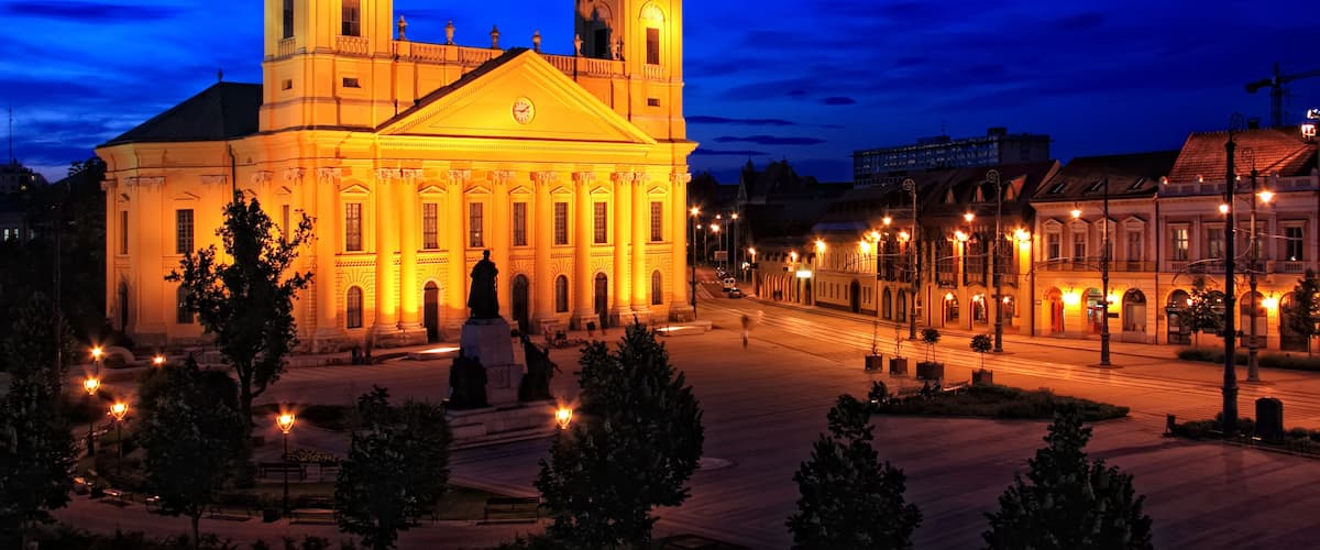 A grand building with two domed towers, illuminated warmly against a twilight sky.