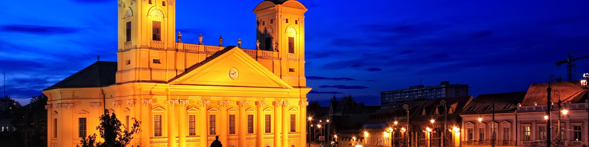 A grand building with two domed towers, illuminated warmly against a twilight sky.