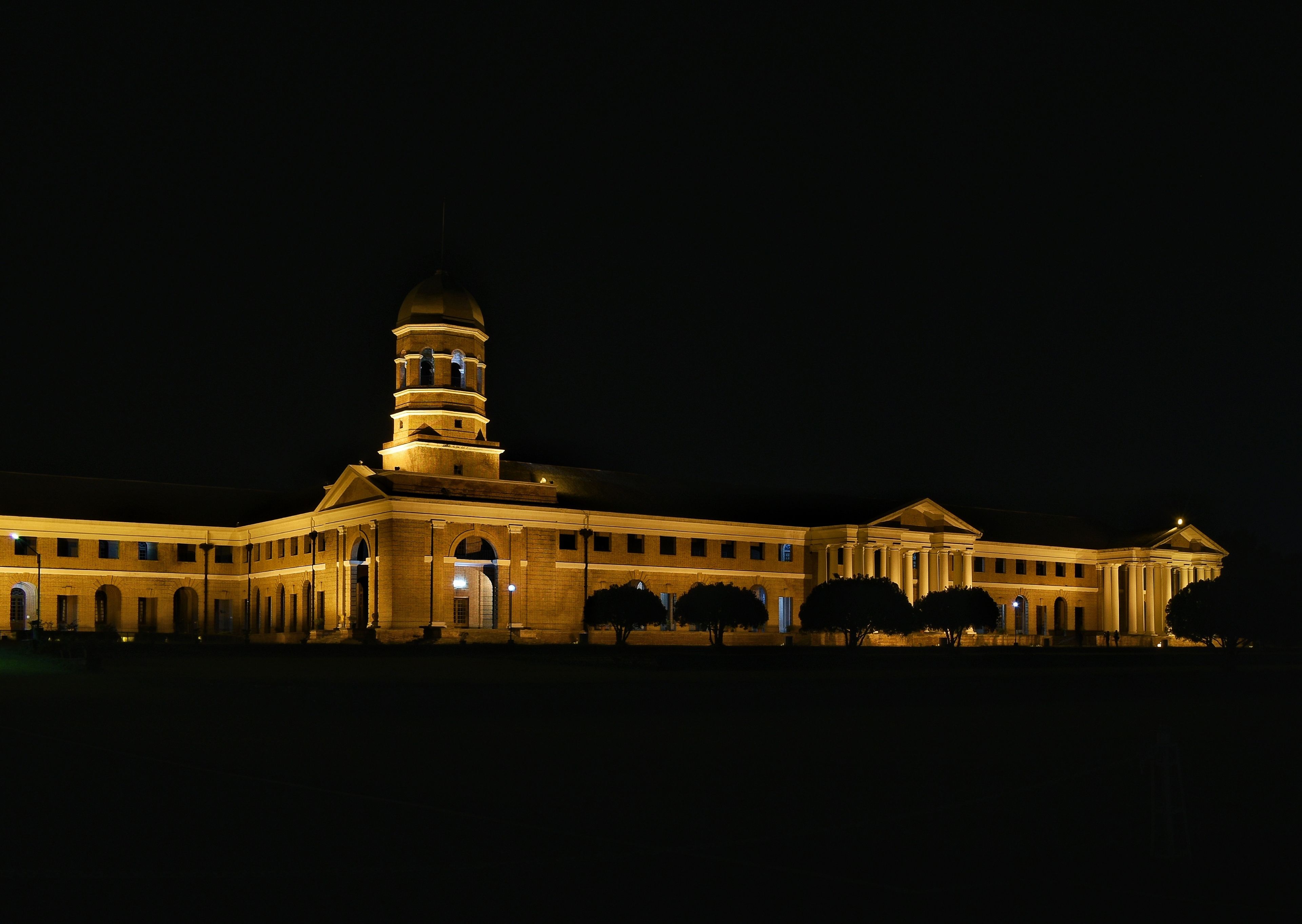 Un edificio grande e iluminado con una torre destacada y varios arcos en su entrada.