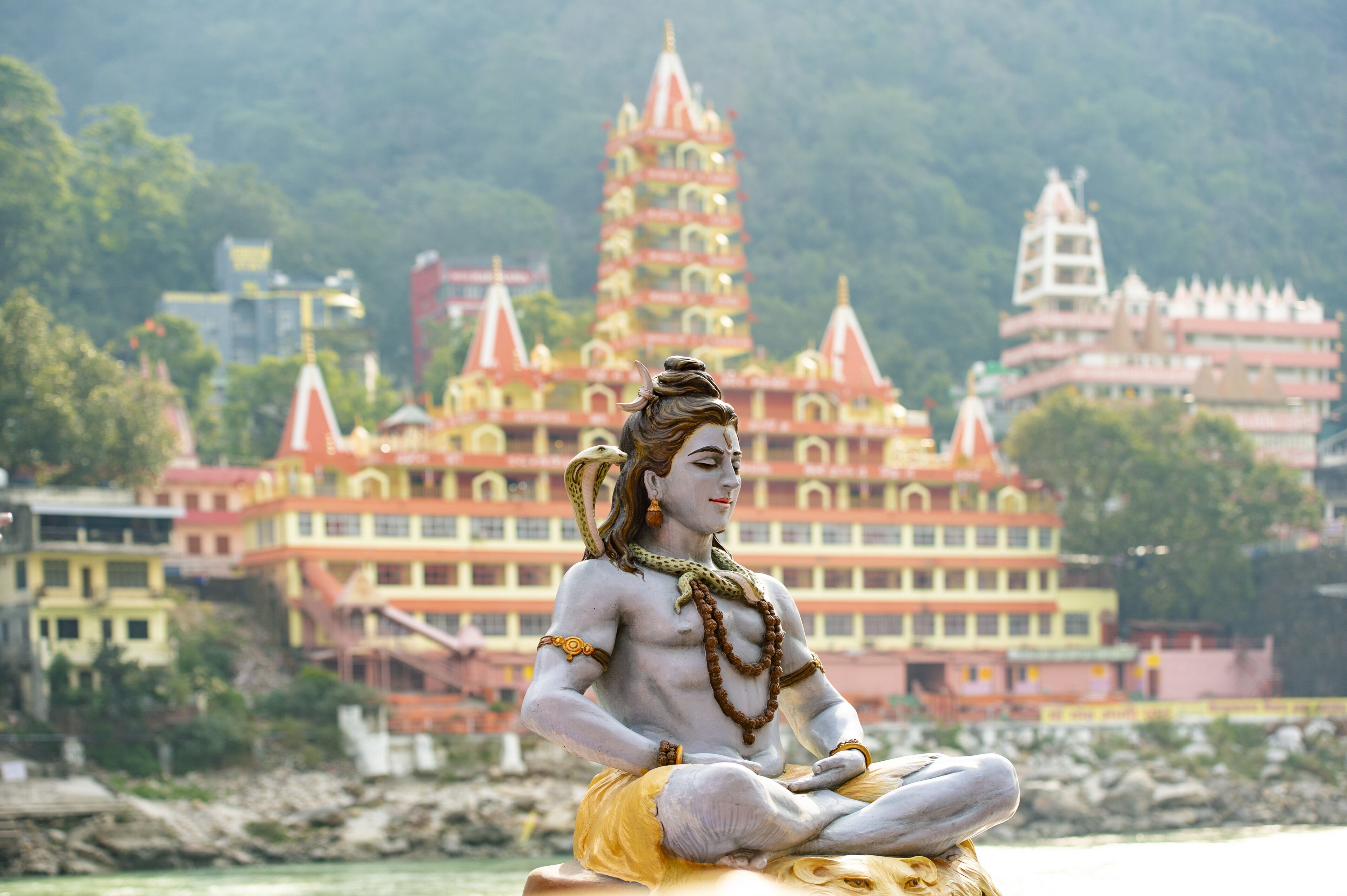 Stunning view of the statue of sitting Lord Shiva on the riverbank of the Ganges river. Blurred Trimbakeshwar Temple in the background. Rishikesh, Uttarakhand, India.