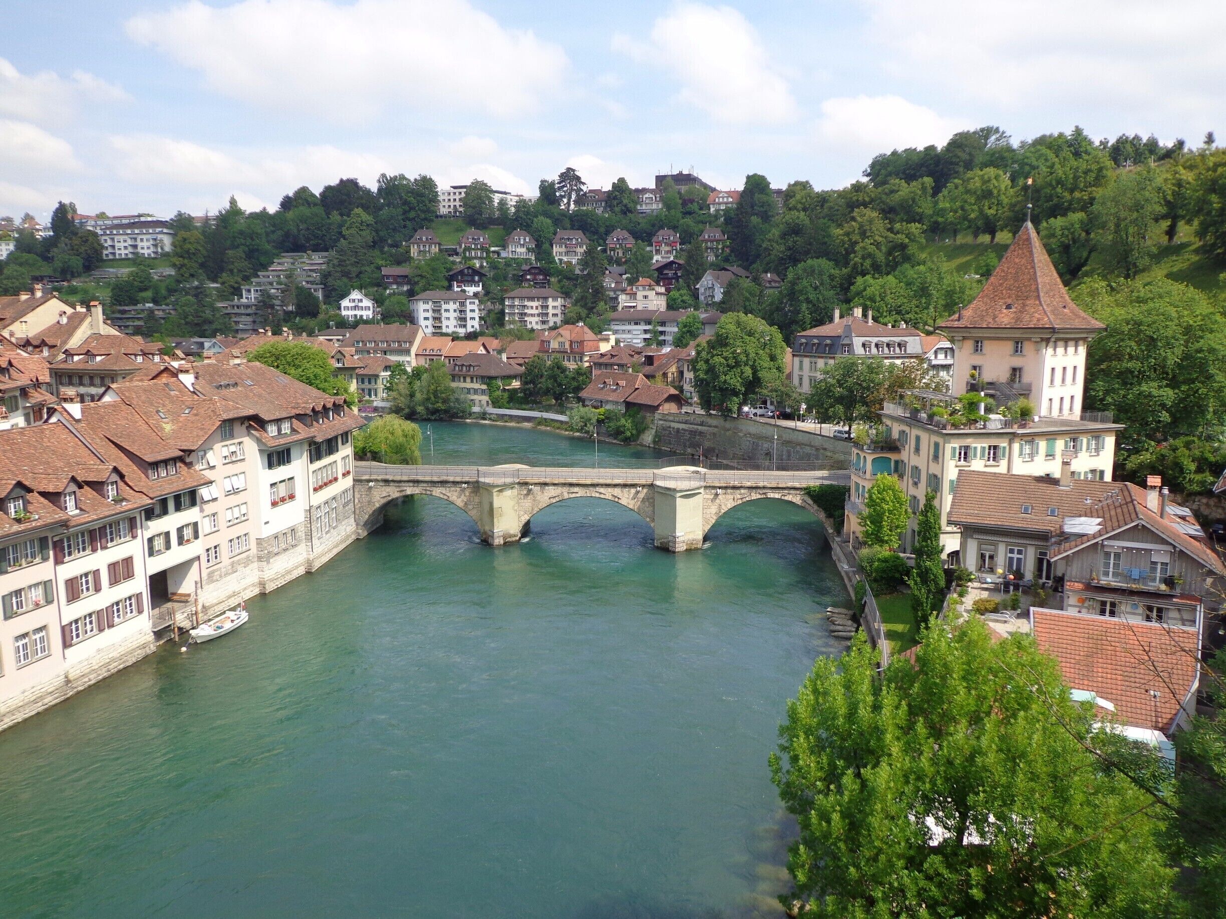 A river with a stone bridge, surrounded by residential buildings and lush greenery.