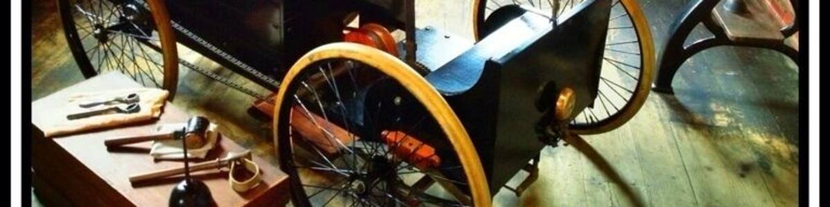 Ein altes Fahrrad mit einem grün gepolsterten Sattel, ein Holztisch mit Werkzeugen und eine Ziegelwand im Hintergrund.