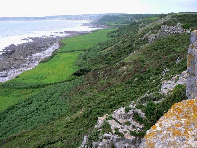 Un paysage côtier avec des champs verdoyants, des falaises rocheuses et une vue sur la mer.