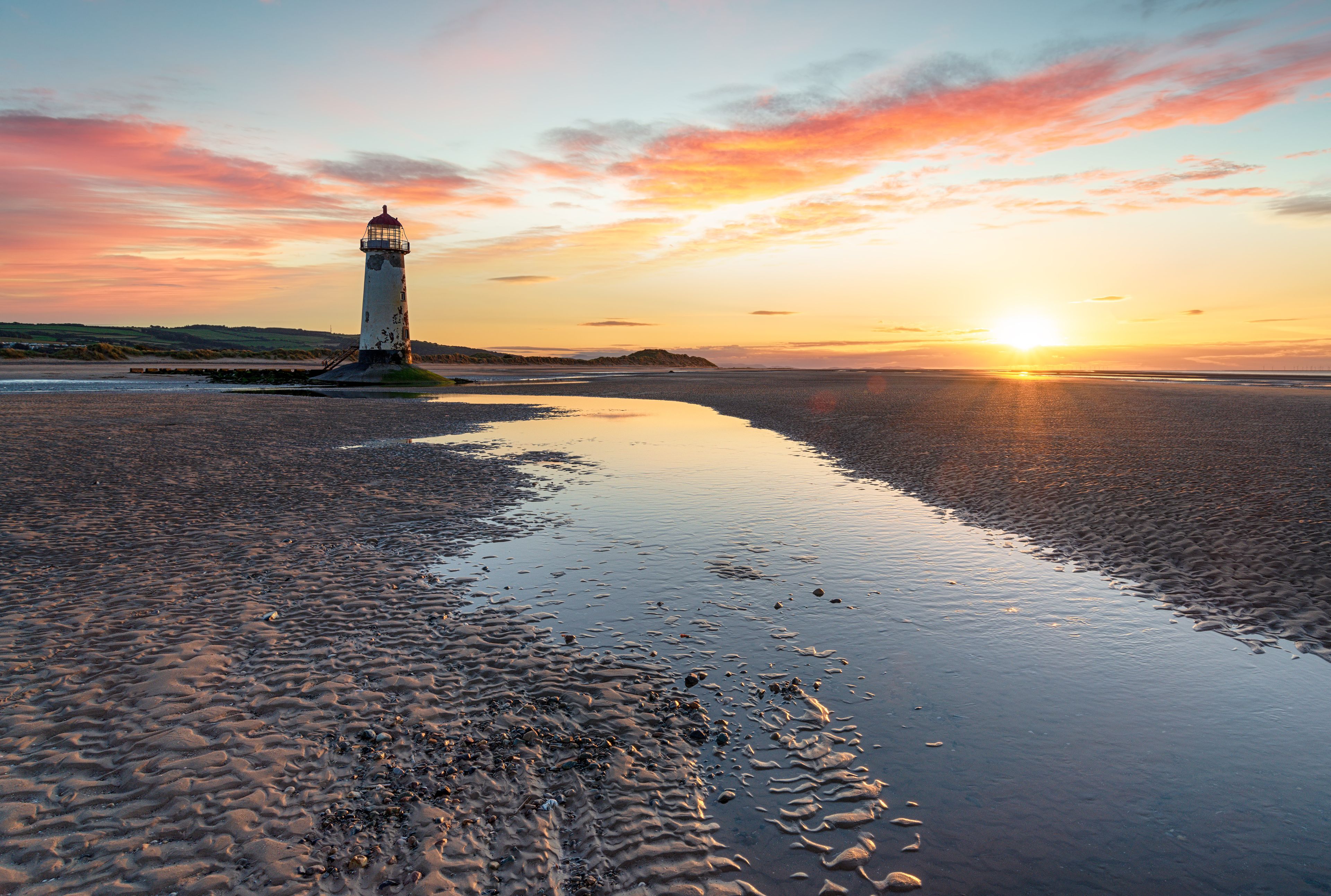 A lighthouse on a beach with a sunset in the background.