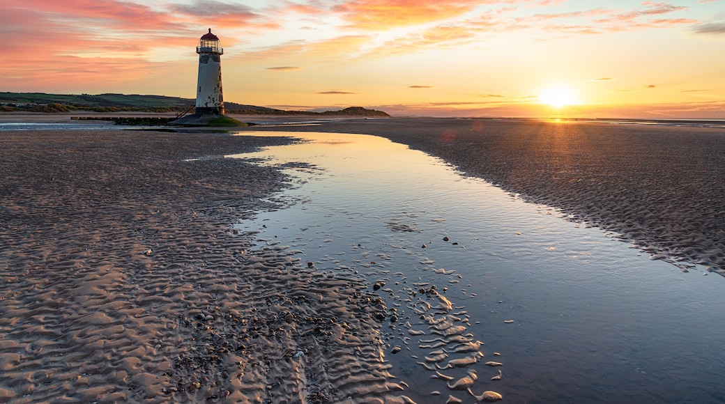 A lighthouse on a beach with a sunset in the background.