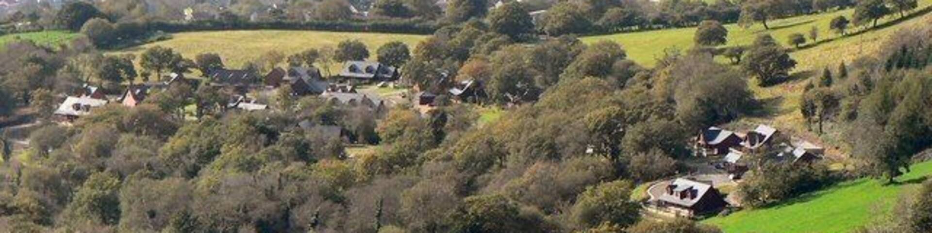 A rural landscape with rolling hills, scattered houses, and dense tree coverage.