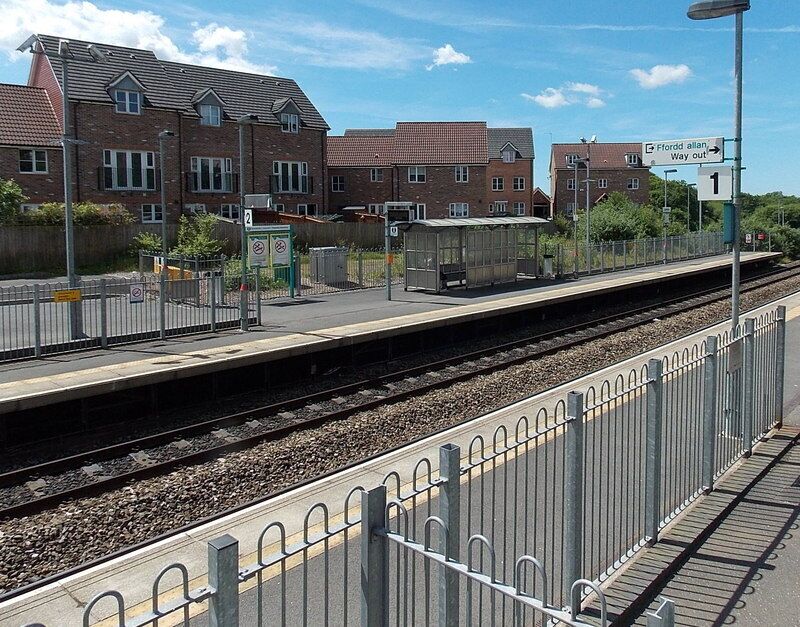 Flat side of Llanharan railway station. Platform 2 on the left is adjacent to flat land on the south side of the station. There is a slope beyond platform 1 on the north side. Access is via steps or ramps. Link
