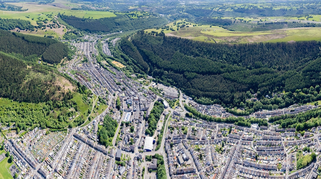 Une vue aérienne d’une ville nichée entre des collines boisées, avec une zone résidentielle dense et une route sinueuse.