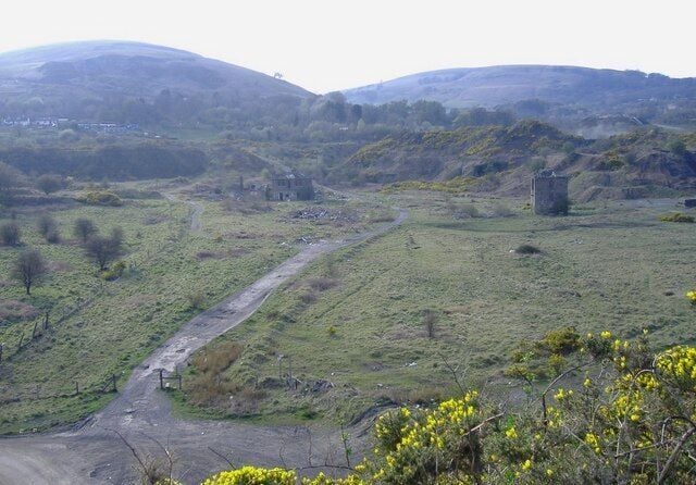 Ländliche Landschaft mit einer Feldweg, sanften Hügeln und einer kleinen Struktur in der Ferne.