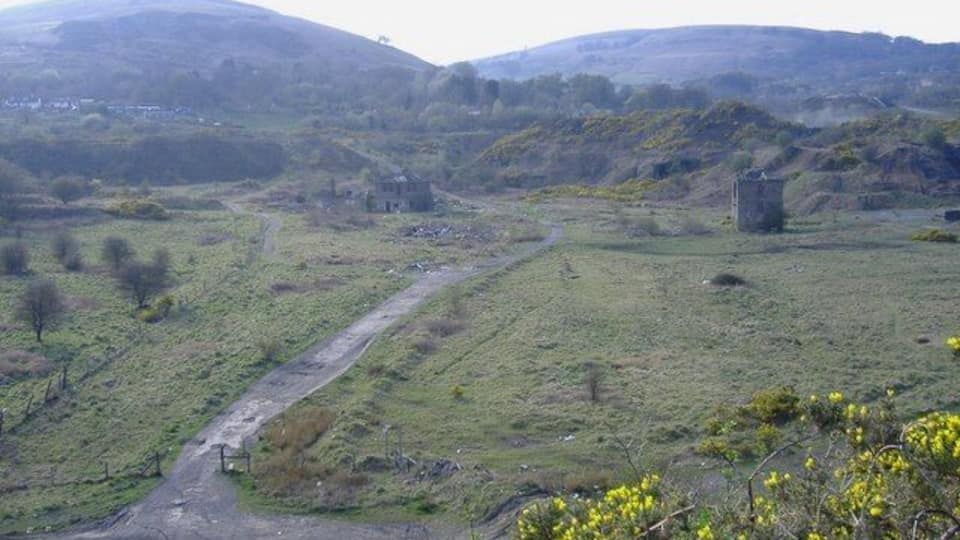 Ländliche Landschaft mit einer Feldweg, sanften Hügeln und einer kleinen Struktur in der Ferne.