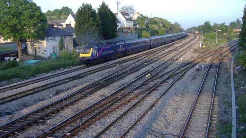 Un tren sobre varias vías, con casas y árboles al fondo.