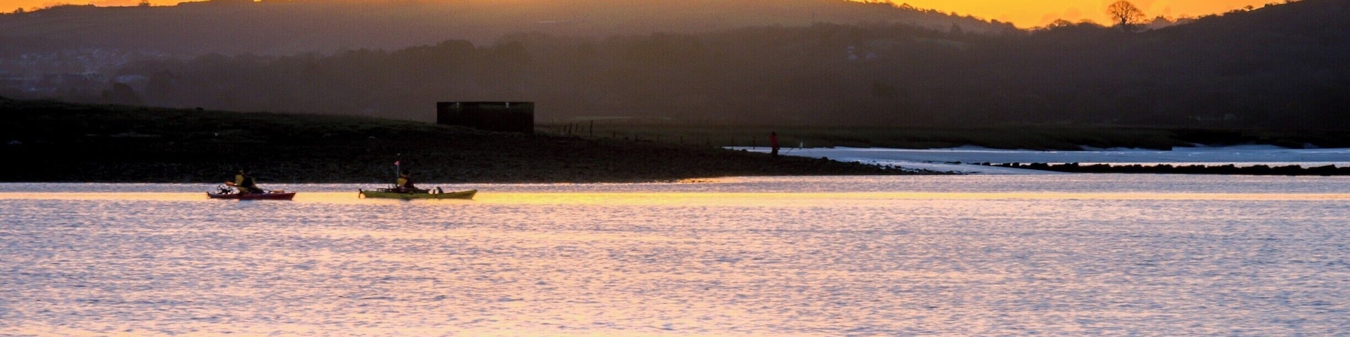 Un atardecer sobre una masa de agua tranquila con barcos y una colina distante.