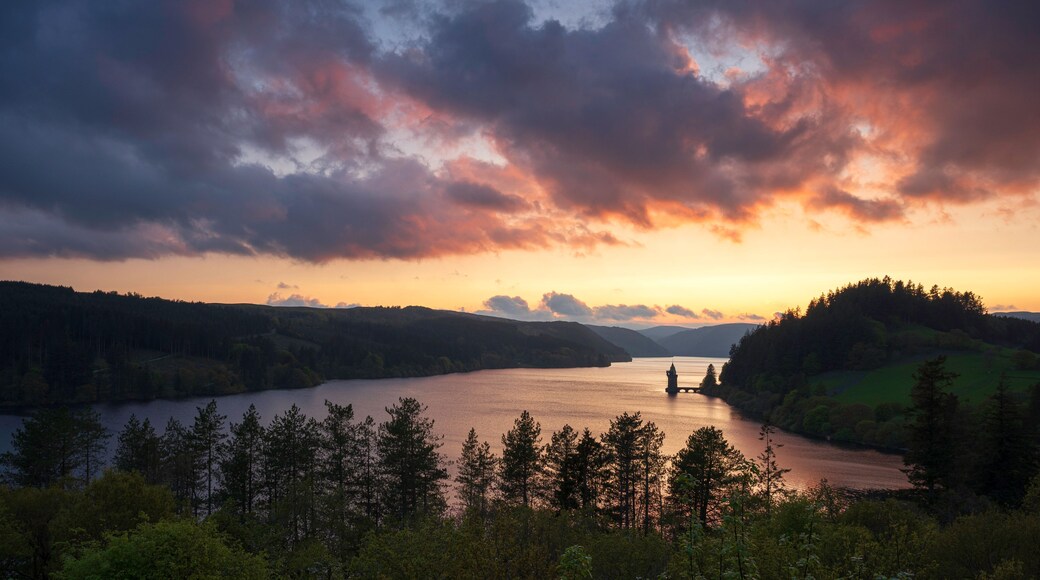 A sunset over a lake surrounded by forested hills.