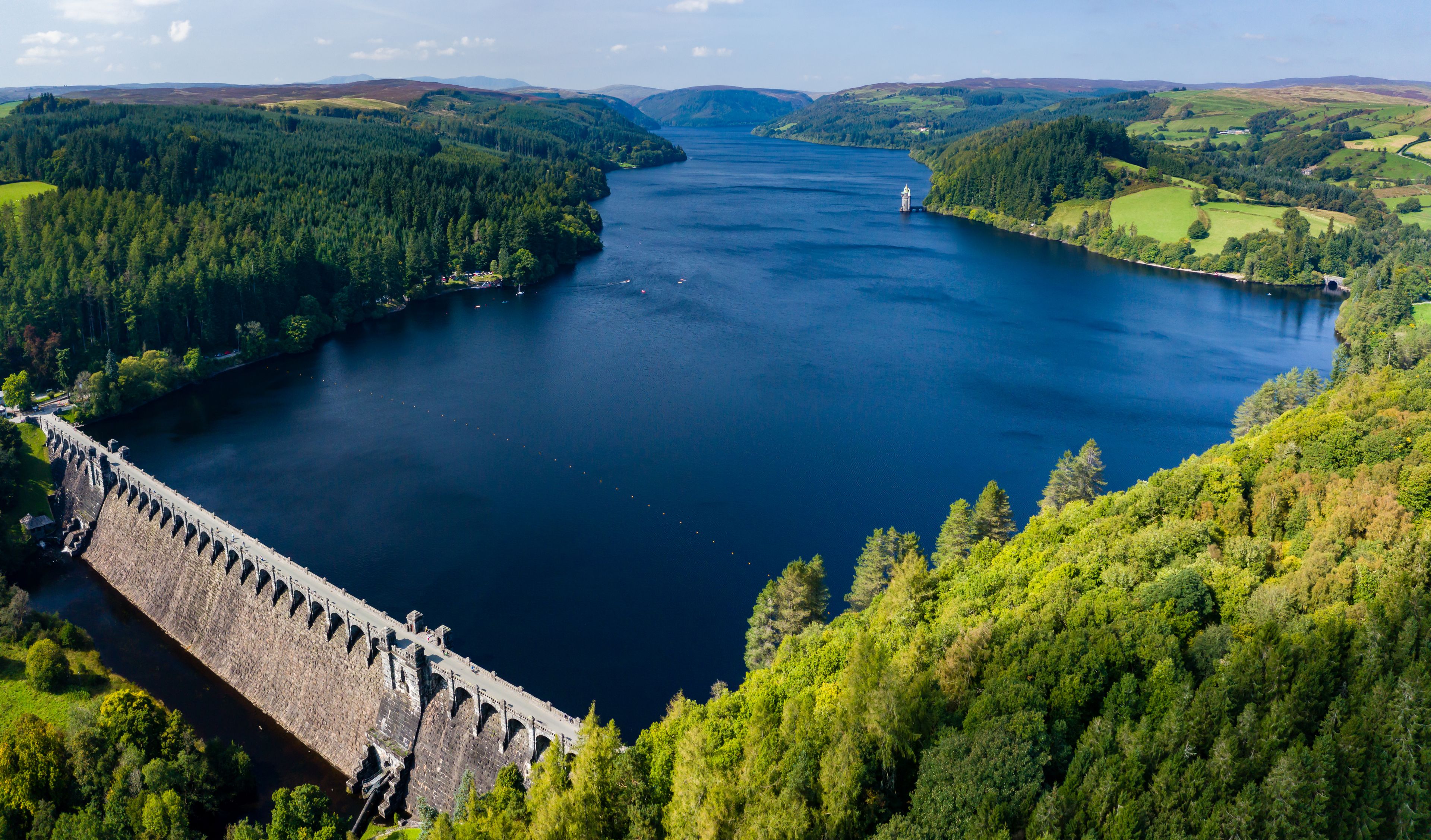 A large dam with multiple gates, surrounded by dense forests and hills.