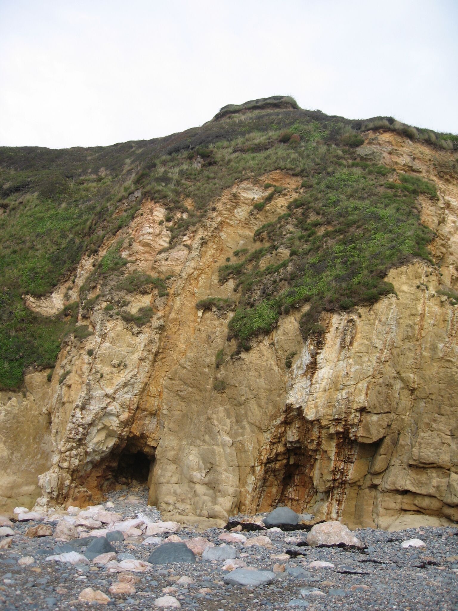 Un acantilado rocoso con la entrada a una cueva y una colina cubierta de hierba.