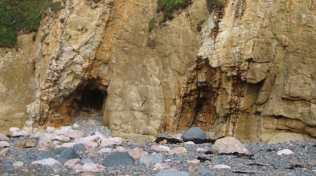 Un acantilado rocoso con la entrada a una cueva y una colina cubierta de hierba.