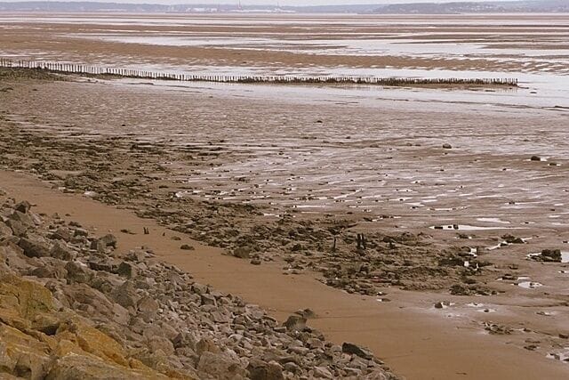 A barren beach with rocky terrain and a wooden fence in the distance.