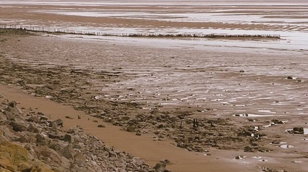 A barren beach with rocky terrain and a wooden fence in the distance.