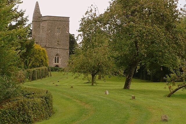 A historic stone tower, a well-maintained lawn, and a large tree in a serene setting.