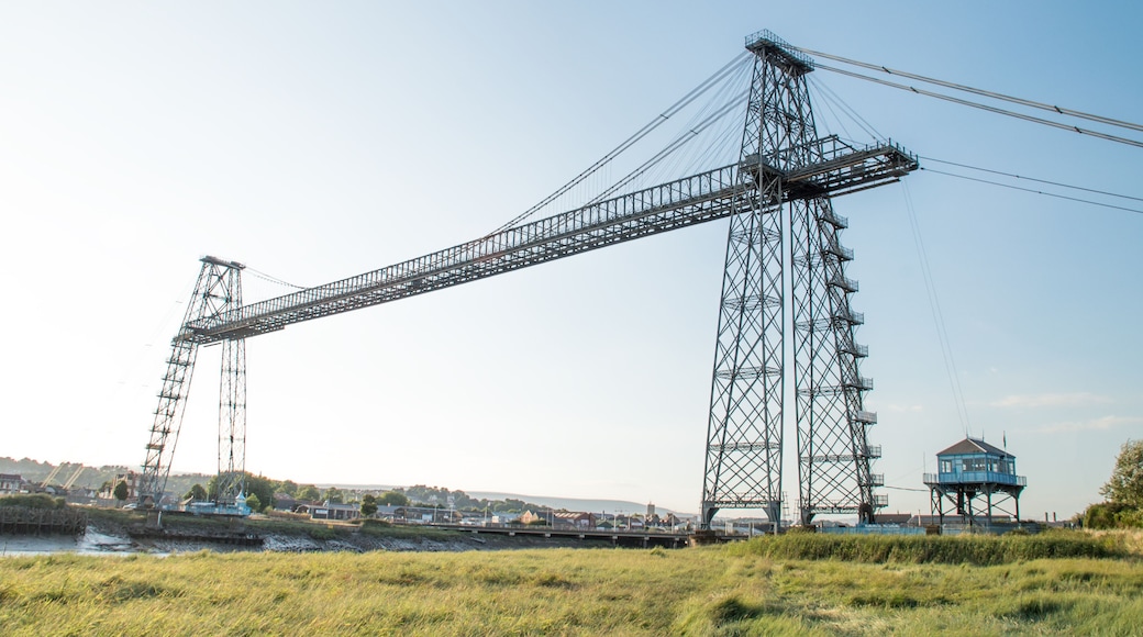 Uma grande ponte de aço com estrutura treliçada complexa, atravessando um corpo de água.