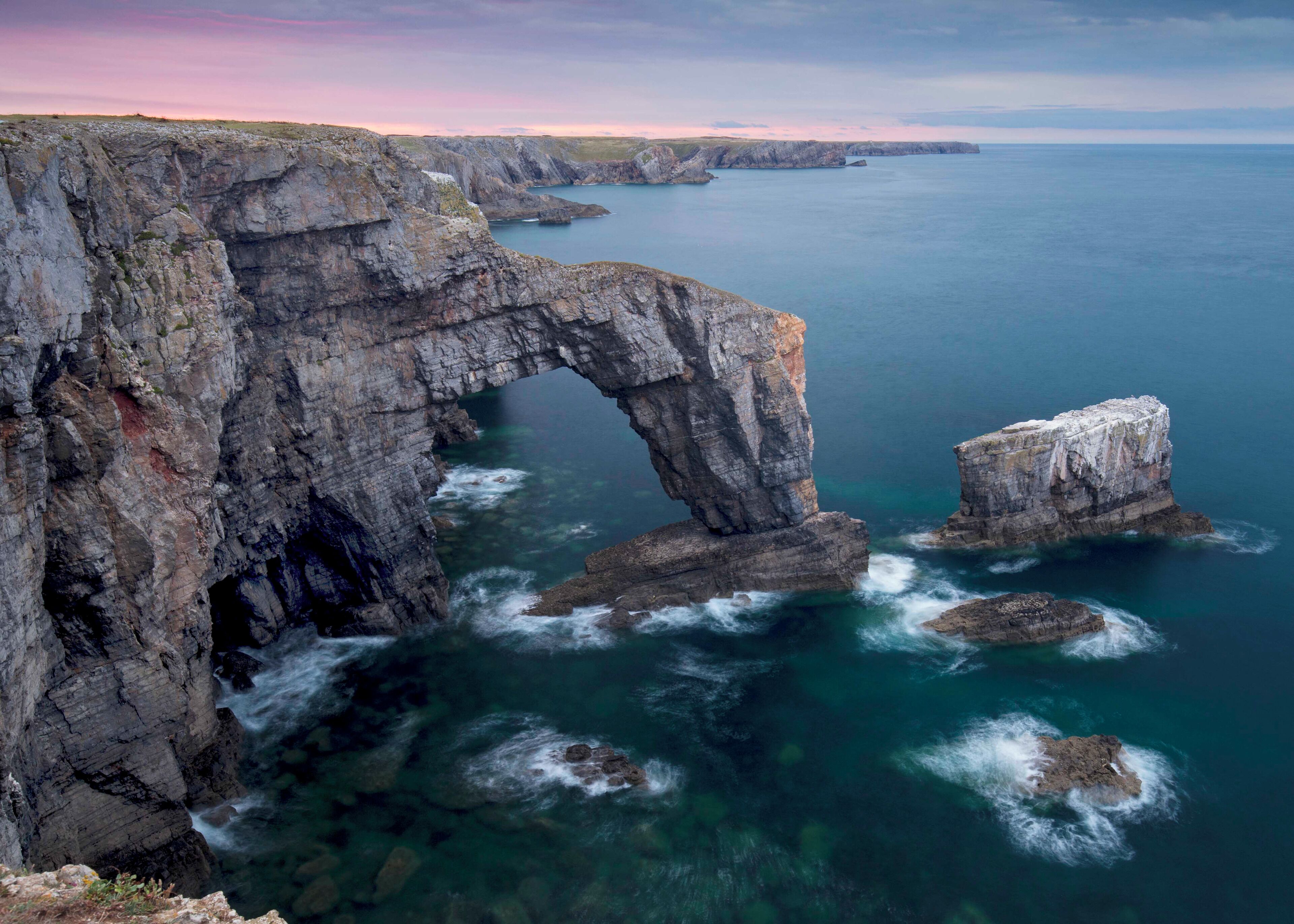 A coastal landscape with a prominent rock arch formation and rugged cliffs.