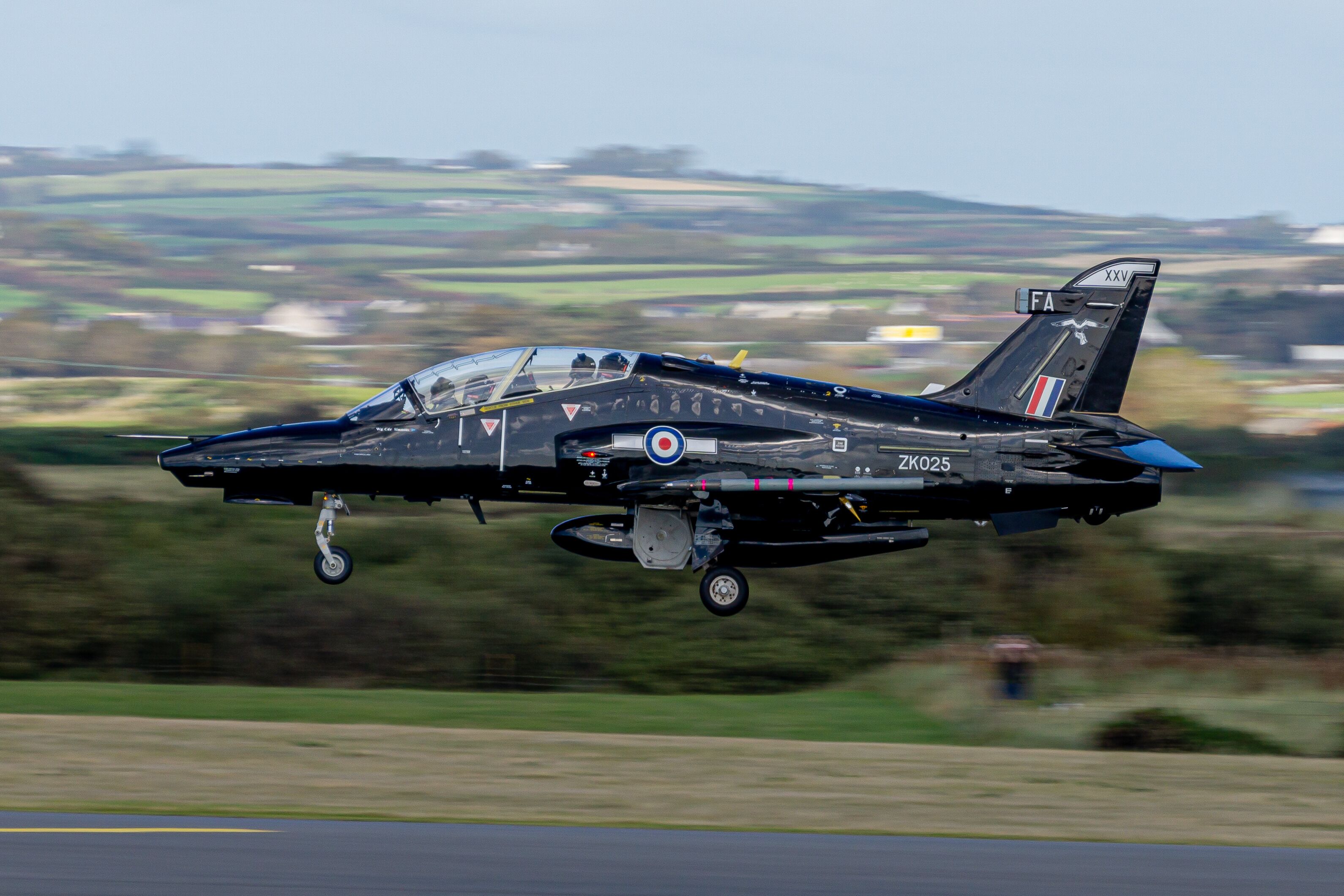 A military jet in flight over a rural landscape.