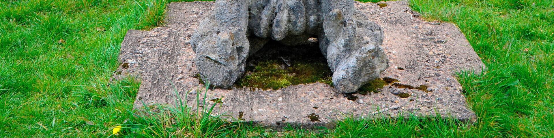 Sculptor Robert Kennedy.
Six separate small upright works set on stone bases; two boxing gloves, two dolls, cherub and a skull. Information from Festival Park: 'The works were carved away from site during 1991. They are made to operate as conventional garden ornamentation, within a constructed garden. The boxing gloves are there to depict some of their associated aspects, such as maleness and competition. The dolls depict something of how an image is idealised for mass consumption, becoming a distortion of the human figure. Both the gloves and the dolls can be seen as gendering devices through role play. The cherub and skull are life and death charms. Each of these suggests ways in which we adopt roles in society. What we really are is never as clear cut as what these images suggest.'
Borderline was supported by Garden Festival Wales and Chapter Arts Centre. 'The sculptor, Robert Kennedy, felt that the Garden Festival was a huge, themed social event in itself. He wanted to create a themed garden within it, something social, commenting to some extent on the diversity of culture within real society.'
A number of sculptures were commissioned for the Garden Festival of Wales in 1991/2 and some works remain on site.