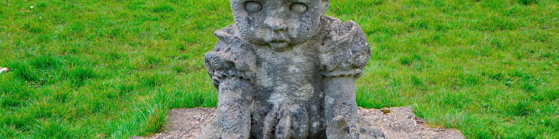 Sculptor Robert Kennedy.
Six separate small upright works set on stone bases; two boxing gloves, two dolls, cherub and a skull. Information from Festival Park: 'The works were carved away from site during 1991. They are made to operate as conventional garden ornamentation, within a constructed garden. The boxing gloves are there to depict some of their associated aspects, such as maleness and competition. The dolls depict something of how an image is idealised for mass consumption, becoming a distortion of the human figure. Both the gloves and the dolls can be seen as gendering devices through role play. The cherub and skull are life and death charms. Each of these suggests ways in which we adopt roles in society. What we really are is never as clear cut as what these images suggest.'
Borderline was supported by Garden Festival Wales and Chapter Arts Centre. 'The sculptor, Robert Kennedy, felt that the Garden Festival was a huge, themed social event in itself. He wanted to create a themed garden within it, something social, commenting to some extent on the diversity of culture within real society.'
A number of sculptures were commissioned for the Garden Festival of Wales in 1991/2 and some works remain on site.