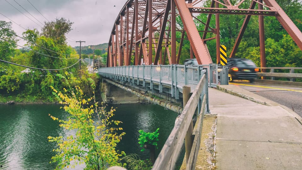 A steel bridge over a river with a car on it.