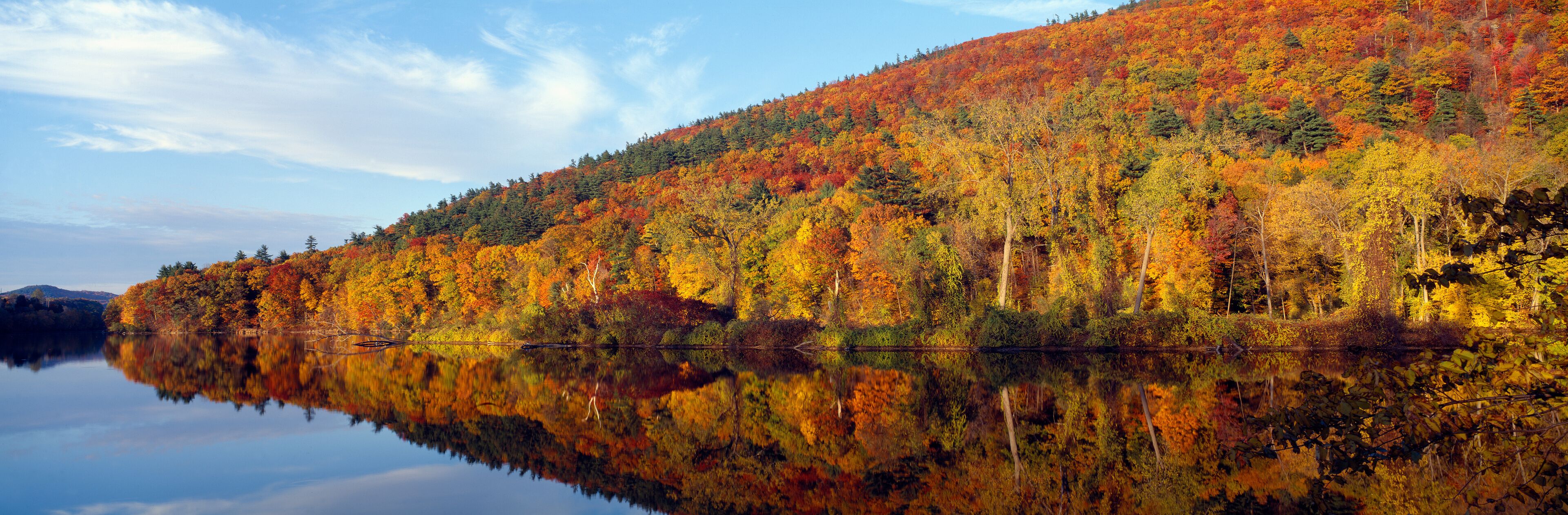 A calm lake reflecting a forest with autumn foliage.