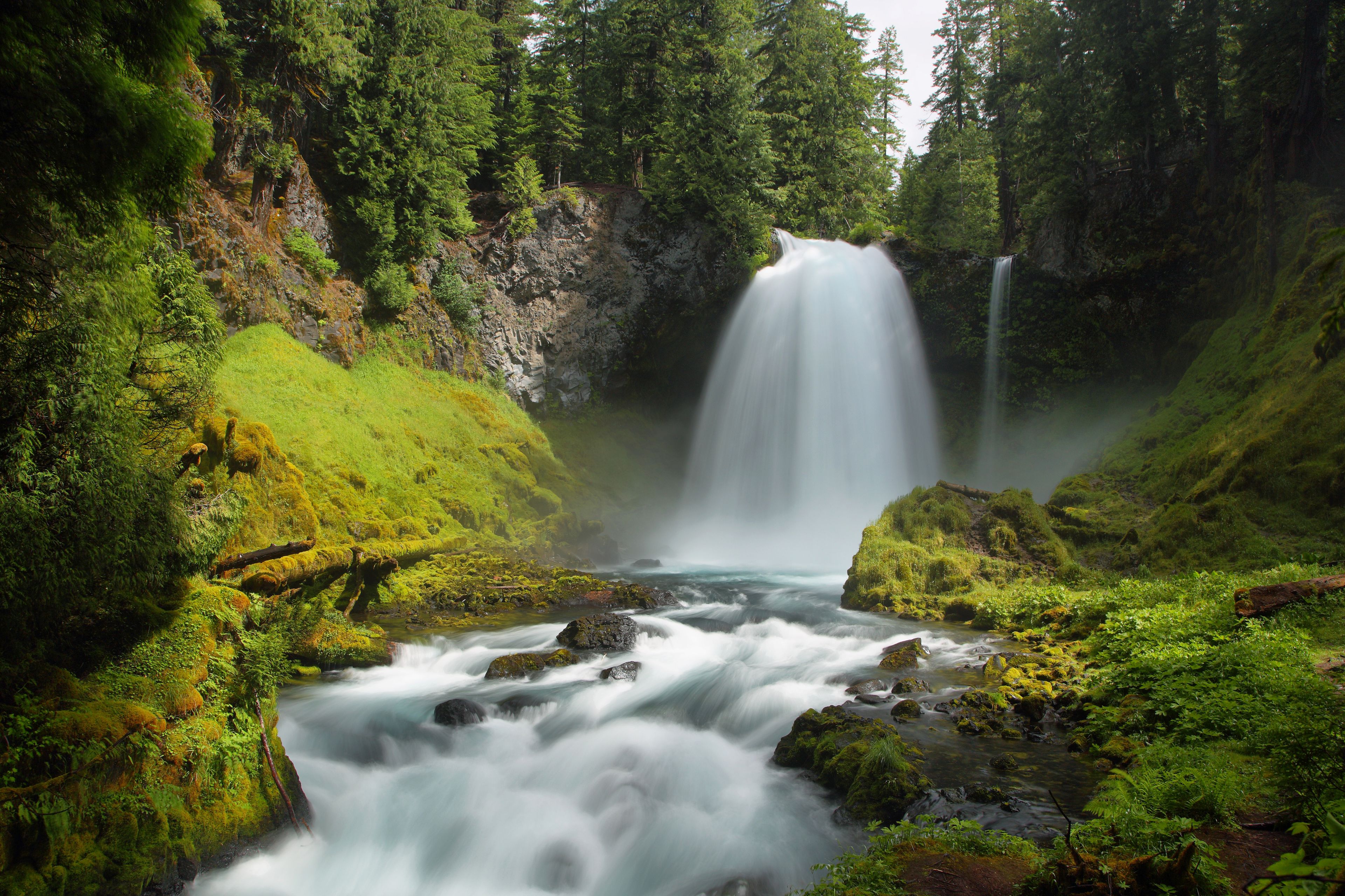 Una cascata che si getta in un fiume, circondata da una vegetazione lussureggiante e ripidi dirupi rocciosi.