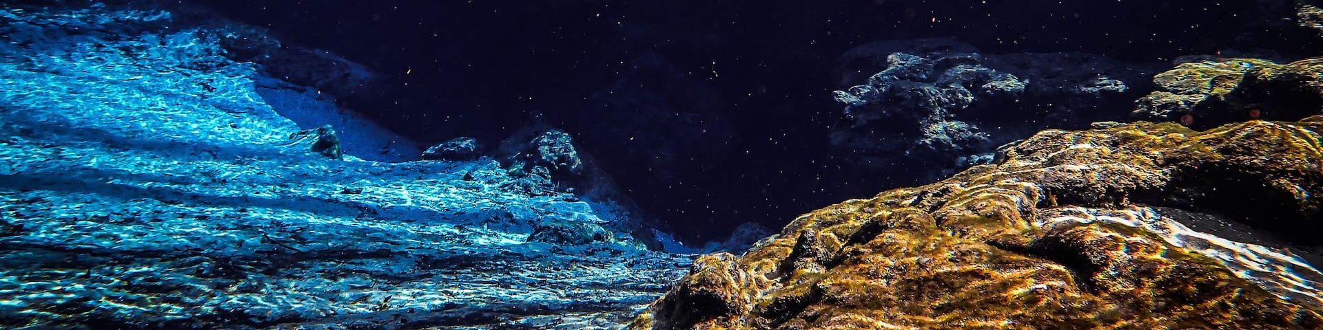 Blue waters of the spring basin drop down to the rocky cavern entrance at Ginnie Ballroom, Ginnie Springs, Florida