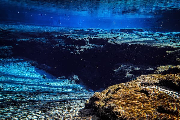Blue waters of the spring basin drop down to the rocky cavern entrance at Ginnie Ballroom, Ginnie Springs, Florida