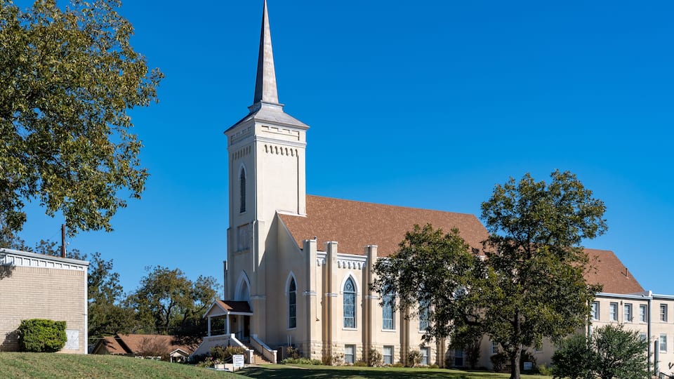 A church with a tall steeple, a brick building to the left, and a well-maintained lawn.