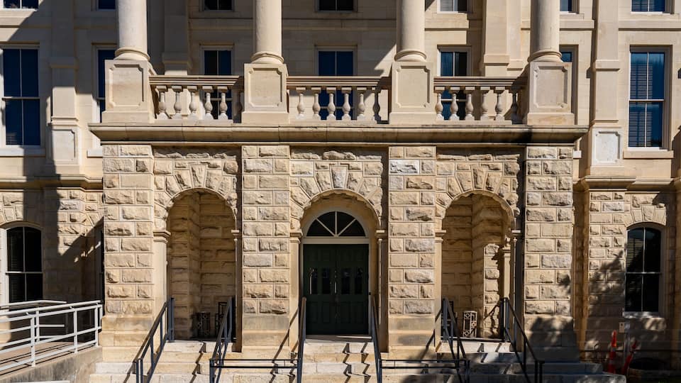 A stone building with a grand entrance, arched doorways, and a balcony with balustrades.