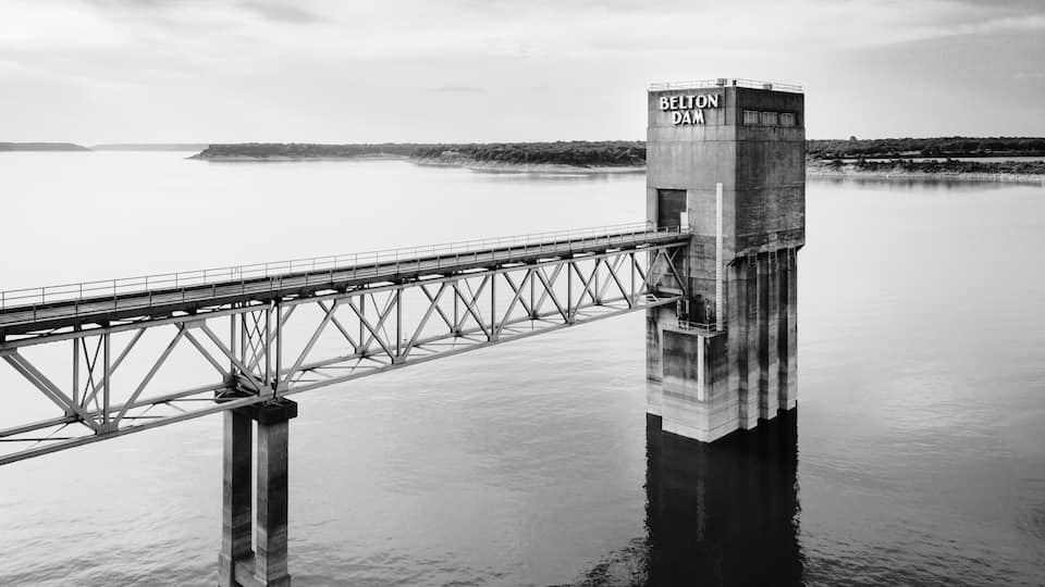 A bridge over calm water with a concrete tower labeled 'BELTON DAM.'