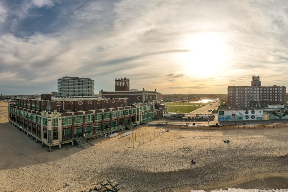 A coastal cityscape with a beach, a large building with a clock tower, and a modern high-rise building.
