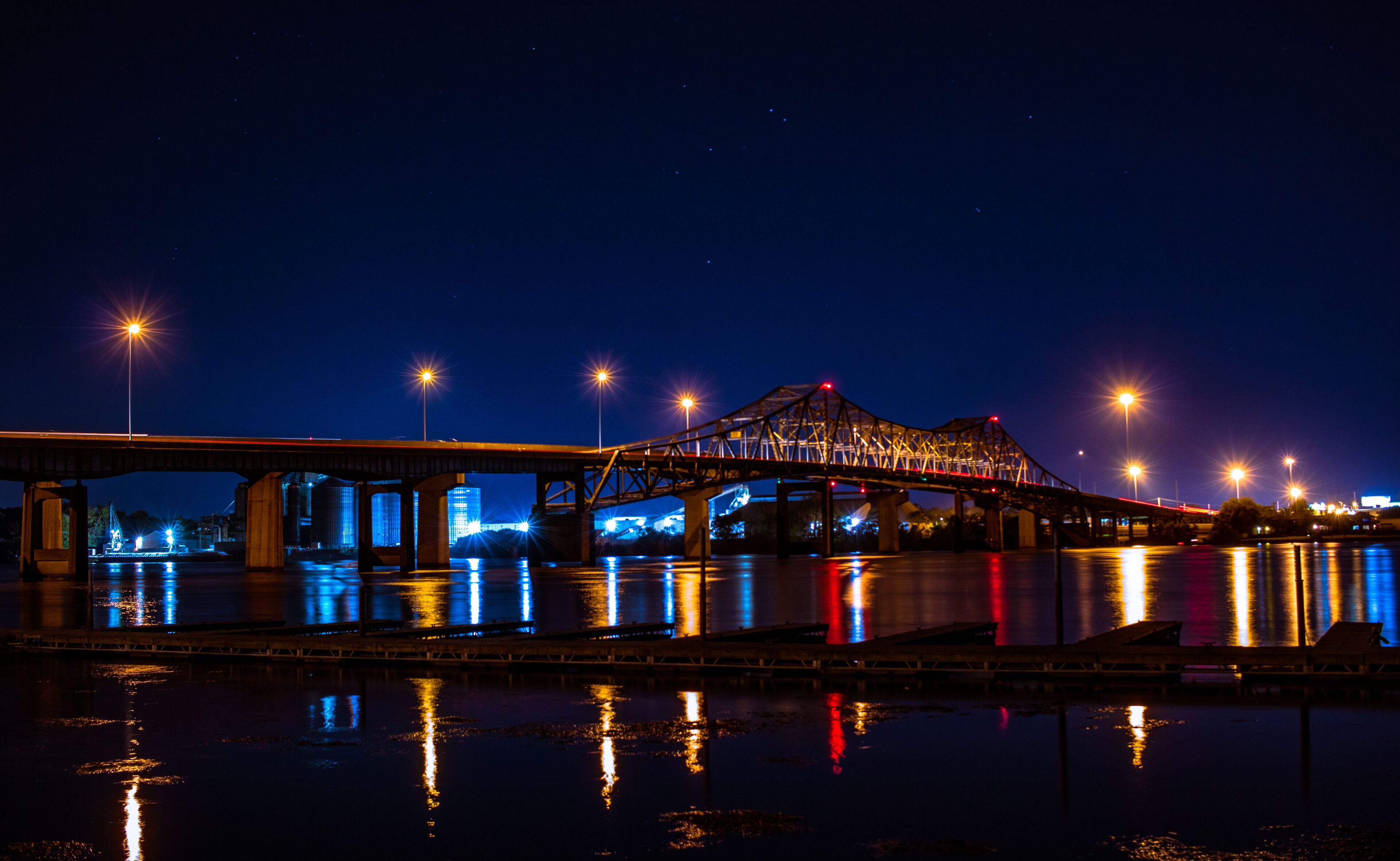 A nighttime view of a bridge over a river with city lights reflecting on the water.