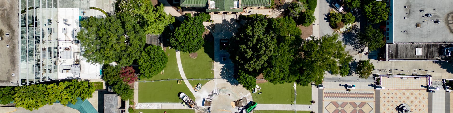 An aerial view of a city with a central green-roofed building surrounded by trees and a circular plaza.