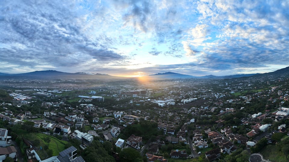 A panoramic view of a city with a sunset over mountains.