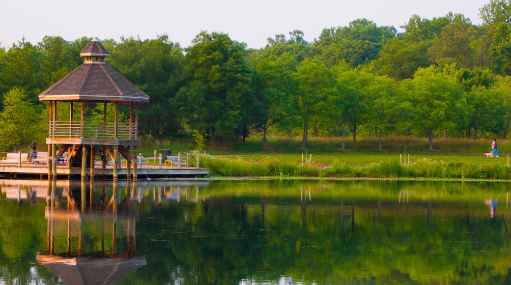 A gazebo on a dock by a calm lake with trees in the background.