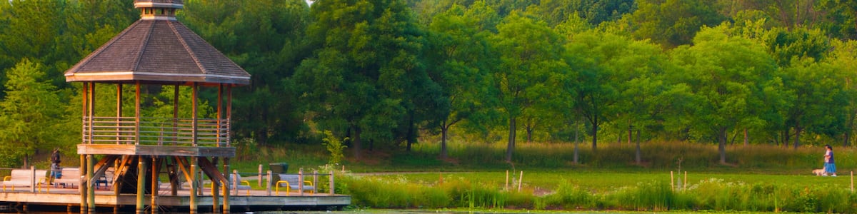 A gazebo on a dock by a calm lake with trees in the background.