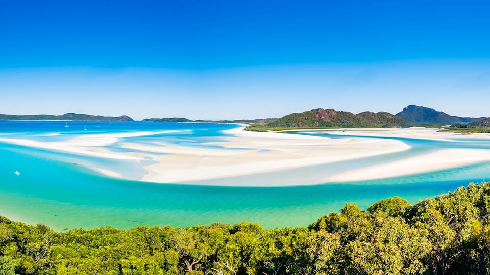 A coastal landscape with white sandy beaches, clear turquoise waters, and lush green hills.
