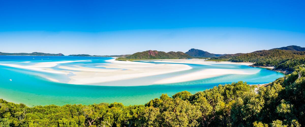 A coastal landscape with white sandy beaches, clear turquoise waters, and lush green hills.