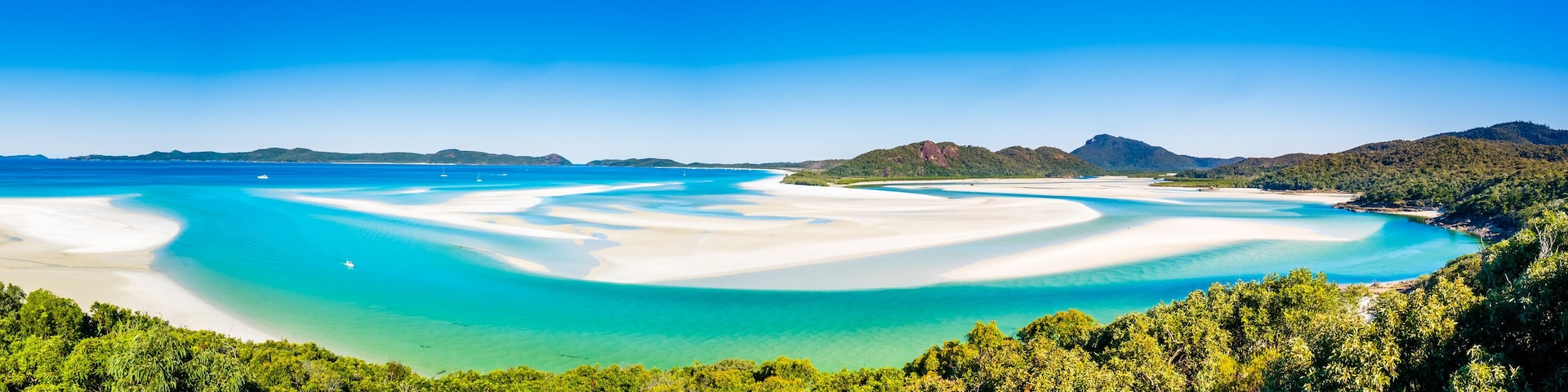 A coastal landscape with white sandy beaches, clear turquoise waters, and lush green hills.