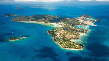 An aerial view of a tropical island with clear turquoise waters, a central peninsula with buildings, and smaller islands in the distance.