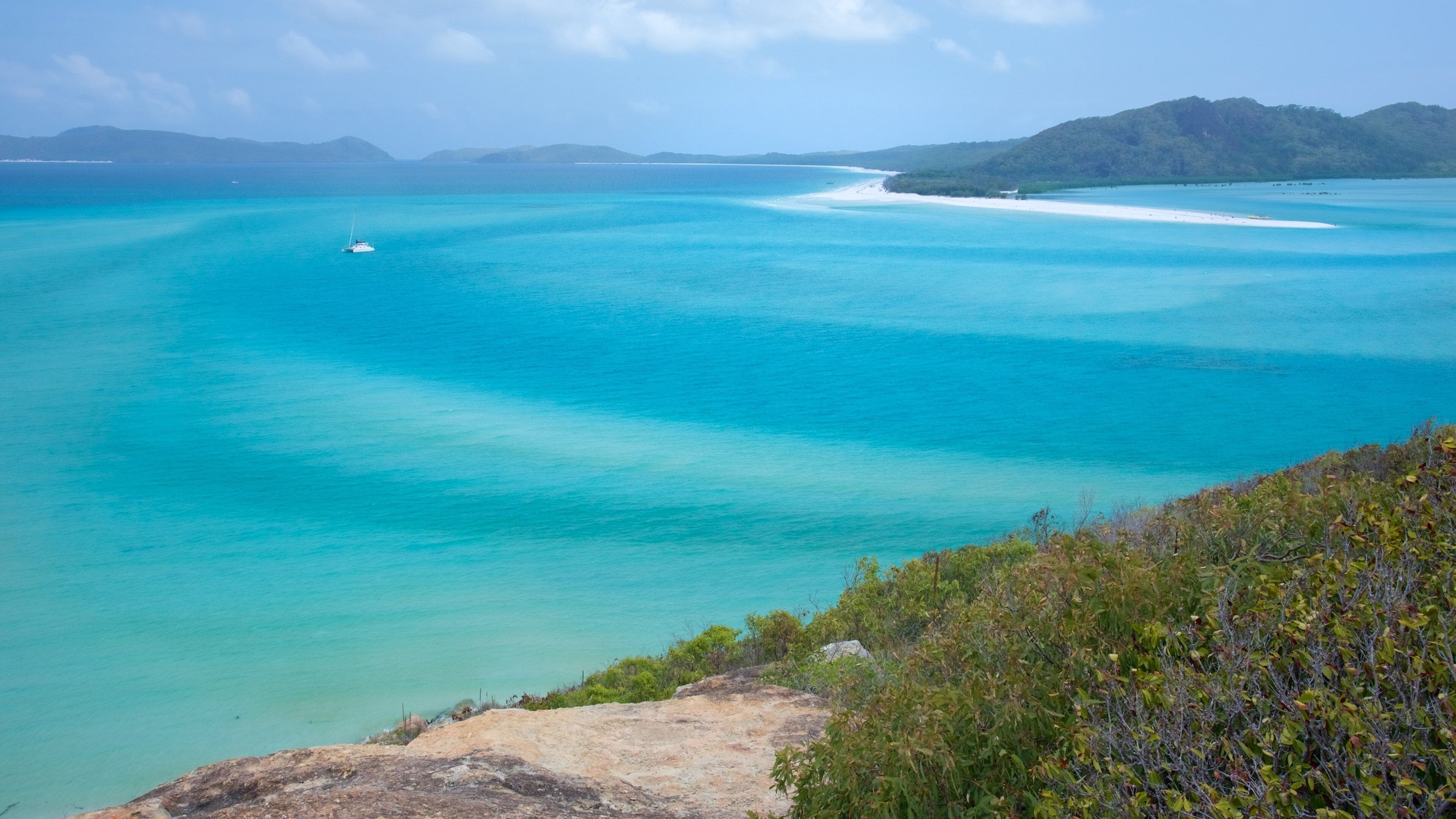 A turquoise sea with a boat, a sandy beach, and green hills.