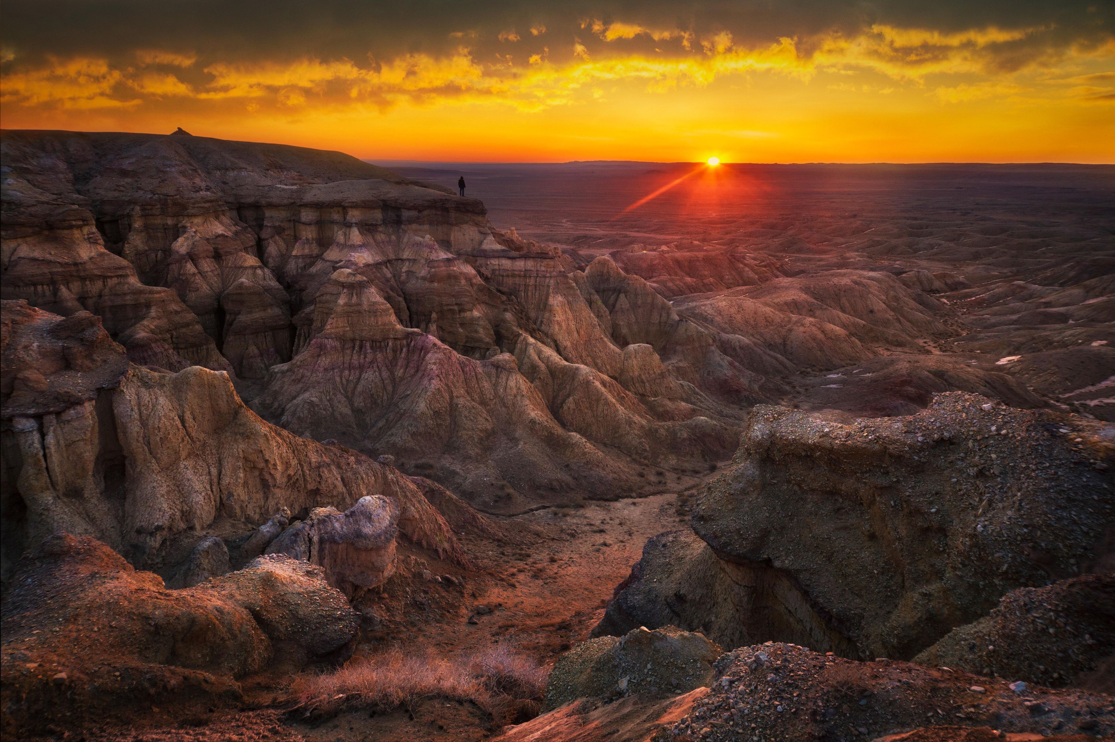 A rugged landscape with eroded rock formations and a sunset in the background.
