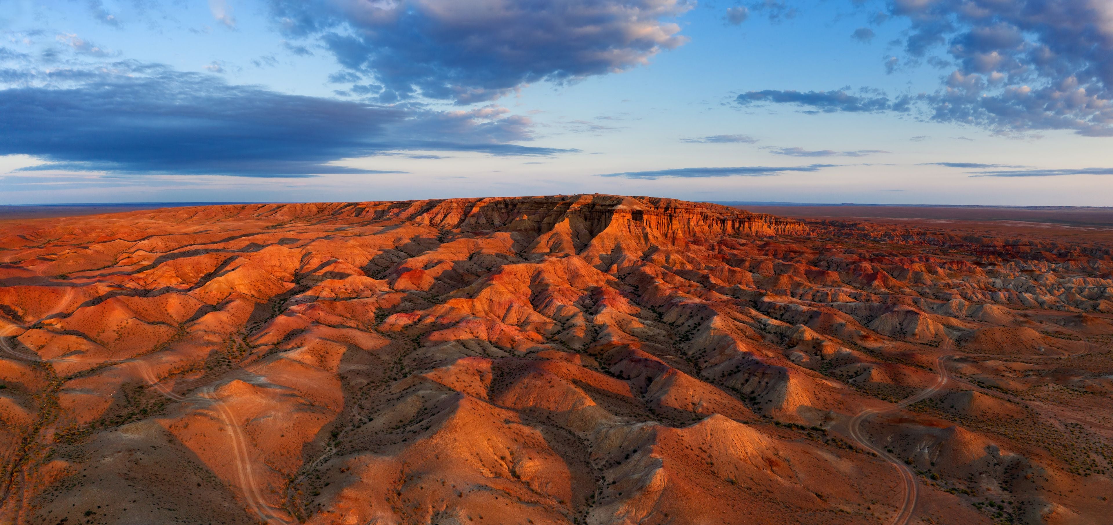 A vast, rugged terrain with layered rock formations and a winding road.