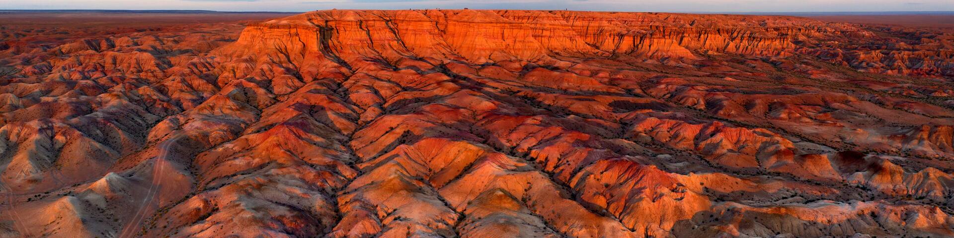 A vast, rugged terrain with layered rock formations and a dramatic sky.